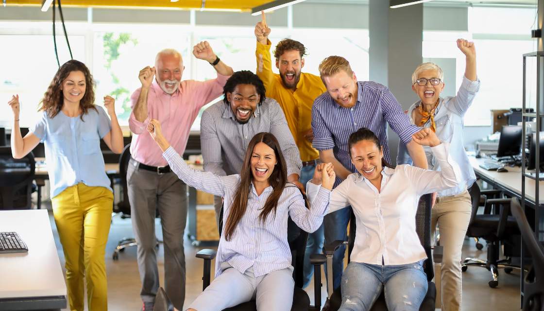 Ein dynamisches Vertriebsteam feiert gemeinsam im Büro, mit strahlenden Gesichtern und hochgerissenen Armen. Humor im Vertrieb zeigt hier seine Wirkung: Eine fröhliche, positive Stimmung stärkt die Teamarbeit und motiviert, gemeinsam große Ziele zu erreichen. Der Spaß an der Arbeit und die lockere Atmosphäre sind ein Paradebeispiel dafür, wie Humor im Vertrieb die Energie und Motivation steigert, was letztlich zu höheren Erfolgsquoten führt.