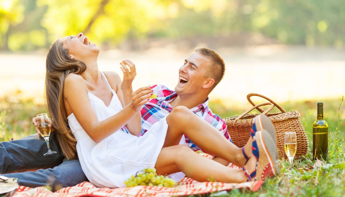 Ein junges Paar lacht gemeinsam bei einem entspannten Picknick im Park und beweist, dass Humor in der Partnerschaft für Leichtigkeit und Nähe sorgt.