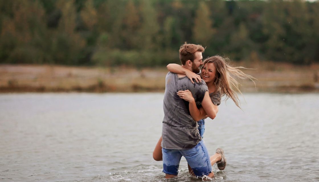 Ein verliebtes Paar genießt einen fröhlichen Moment im Wasser, lacht und zeigt, dass Humor in der Partnerschaft der Schlüssel zu unbeschwerten Erinnerungen ist.