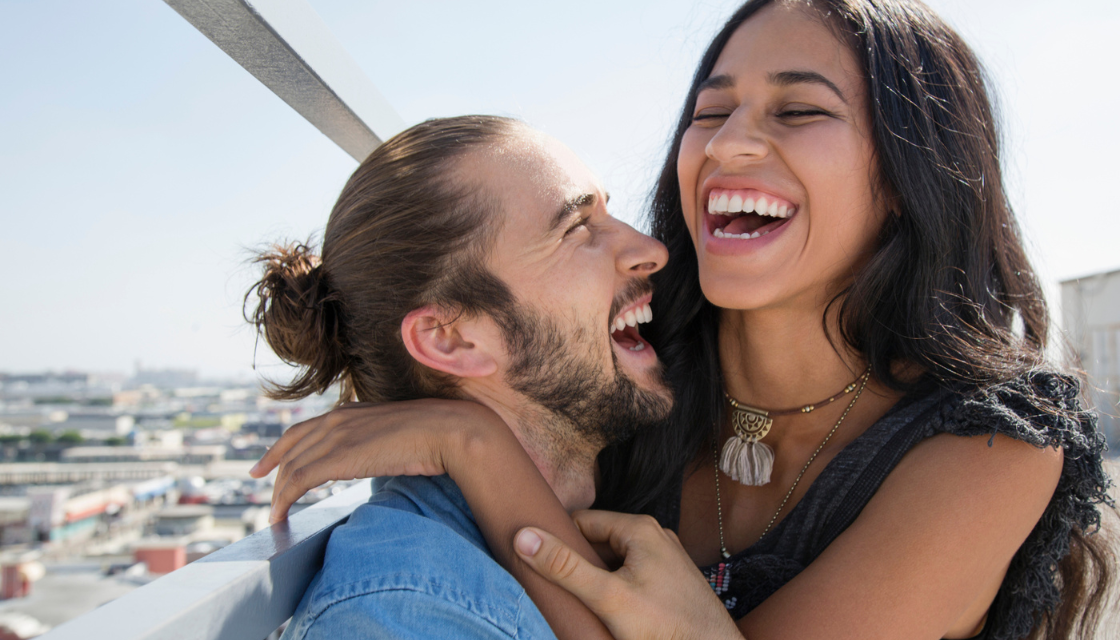 Ein glueckliches Paar lacht herzlich miteinander und umarmt sich – visuelles Beispiel dafuer, wie Humor macht attraktiv und echte Verbindung schafft.