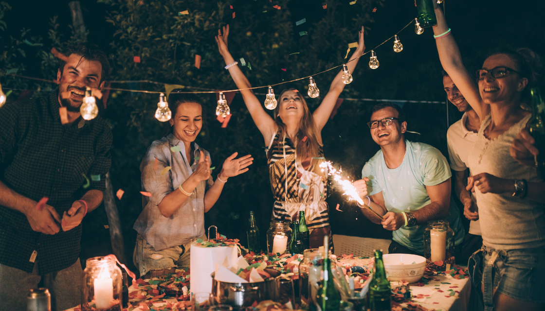 Eine Gruppe Menschen feiert ausgelassen unter Lichterketten und zeigt, wie soziale Kontakte zu den wichtigsten mentalen Gesundheit Tipps gehören. Gemeinsames Lachen und Verbindung reduzieren Stress und stärken das emotionale Wohlbefinden.