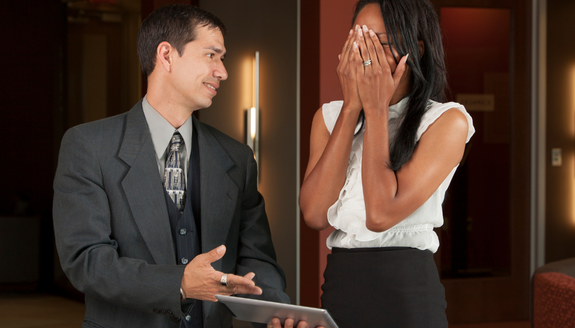 Eine Frau verdeckt im Business-Umfeld ihr Gesicht, während ein Mann neben ihr spricht. Solche Momente zeigen, warum viele ihr Lachen verbessern wollen, um souveräner aufzutreten.