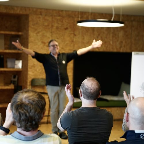 Mann in grauer Hose und schwarzem kurzärmligem Shirt jubelt fröhlich beim Humor Coaching für Führungskräfte Workshop